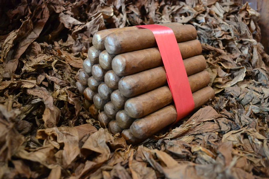 This is a image of a stack of 20 to 25 cigars. They are Rapped together with a thin colored paper ranging from cool whites to firey red wrappings they are forming a trianglur shape simular to a mountain or pyramid. While the Background shows the cigars placed on a feild of tabaco.