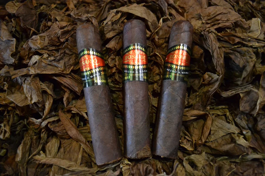 This is a image of a stack of 1 to 5 cigars. They are layed on a of Background feild of tabaco. the cigars are very dark in color like a dark coffee color.