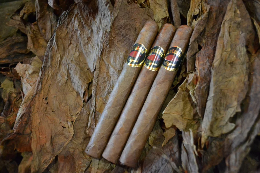 This is a image of a stack of 1 to 5 cigars. They are layed on a of Background feild of tabaco.