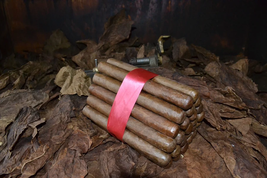 This is a image of a stack of 20 to 25 cigars. They are Rapped together with a thin colored paper ranging from cool whites to firey red wrappings they are forming a trianglur shape simular to a mountain or pyramid. While the Background shows the cigars placed on a feild of tabaco.