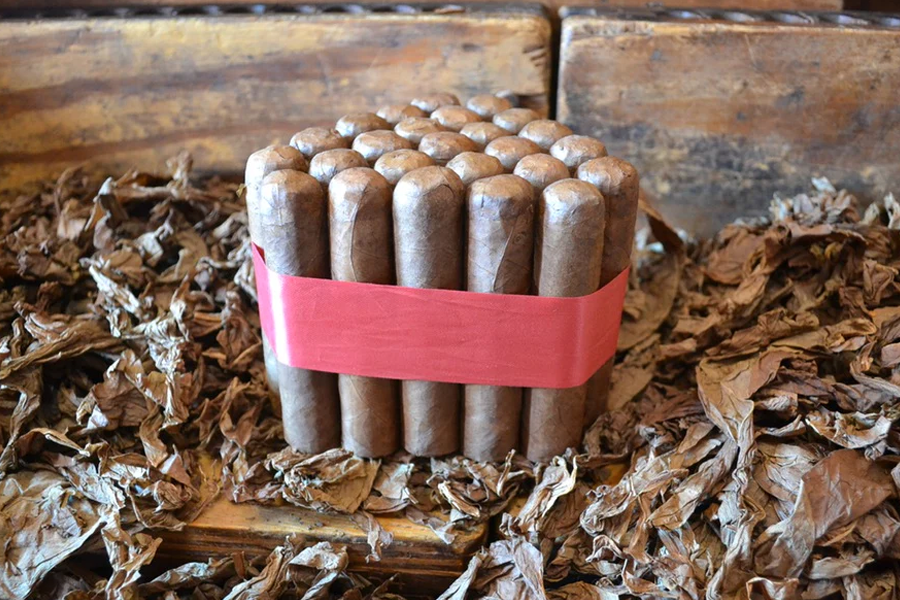 This is a image of a stack of 20 to 25 cigars. They are Rapped together with a thin colored paper ranging from cool whites to firey red wrappings they are forming a trianglur shape simular to a mountain or pyramid. While the Background shows the cigars placed on a feild of tabaco.