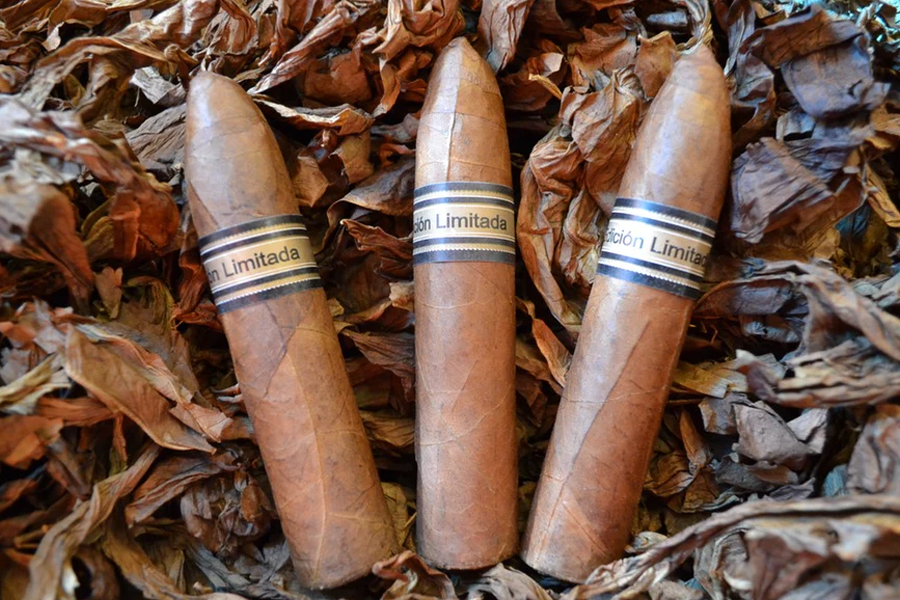 This is a image of a stack of 1 to 5 cigars. They are layed on a of Background feild of tabaco. The cigars are stubby and pointed at the top.