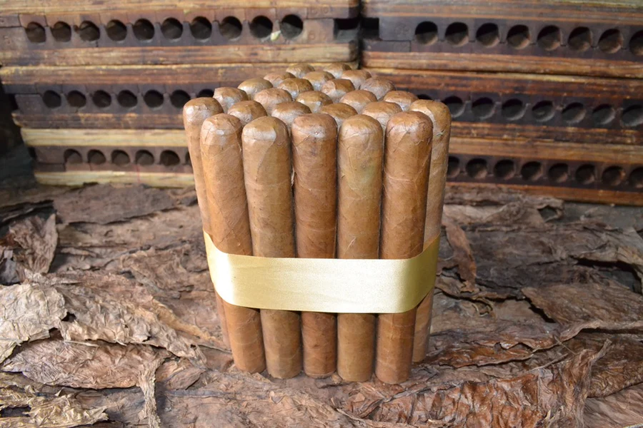 This is a image of a stack of 20 to 25 cigars. They are Rapped together with a thin colored paper ranging from cool whites to firey red wrappings they are forming a trianglur shape simular to a mountain or pyramid. While the Background shows the cigars placed on a feild of tabaco.