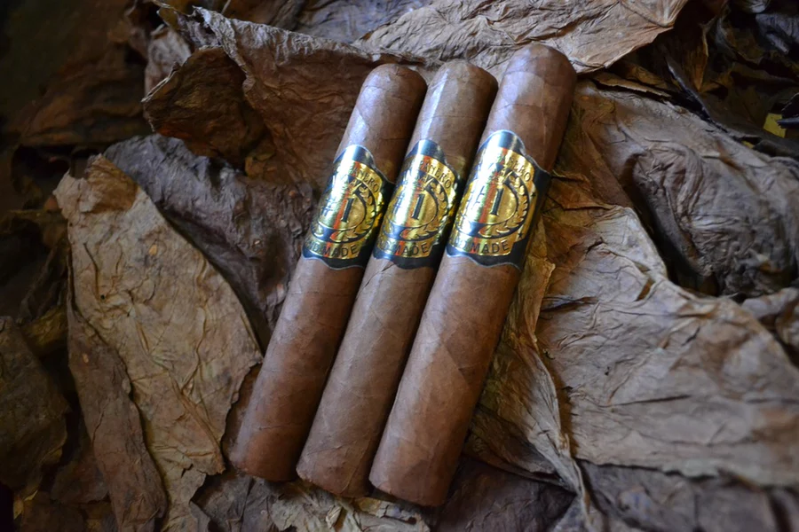 This is a image of a stack of 1 to 5 cigars. They are layed on a of Background feild of tabaco.
