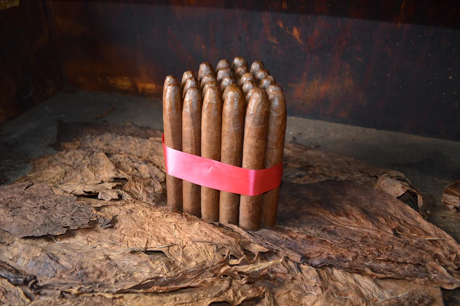 This is a image of a stack of 20 to 25 cigars. They are Rapped together with a thin colored paper ranging from cool whites to firey red wrappings they are forming a trianglur shape simular to a mountain or pyramid. While the Background shows the cigars placed on a feild of tabaco.