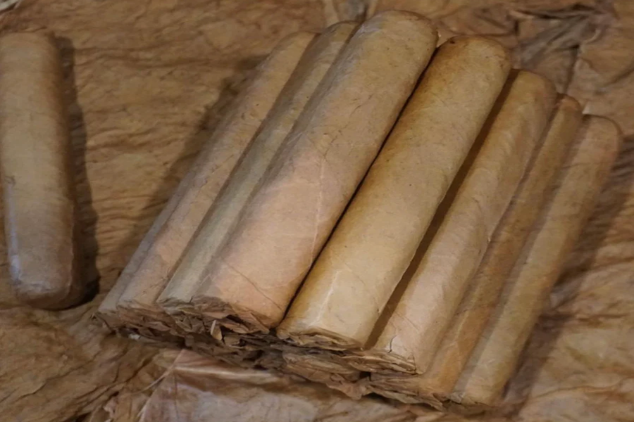 This is a image of a stack of 20 to 25 cigars. They are Rapped together with a thin colored paper ranging from cool whites to firey red wrappings they are forming a trianglur shape simular to a mountain or pyramid. While the Background shows the cigars placed on a feild of tabaco.