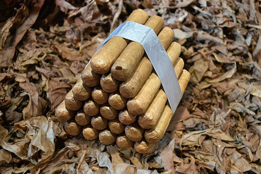 This is a image of a stack of 20 to 25 cigars. They are Rapped together with a thin colored paper ranging from cool whites to firey red wrappings they are forming a trianglur shape simular to a mountain or pyramid. While the Background shows the cigars placed on a feild of tabaco.