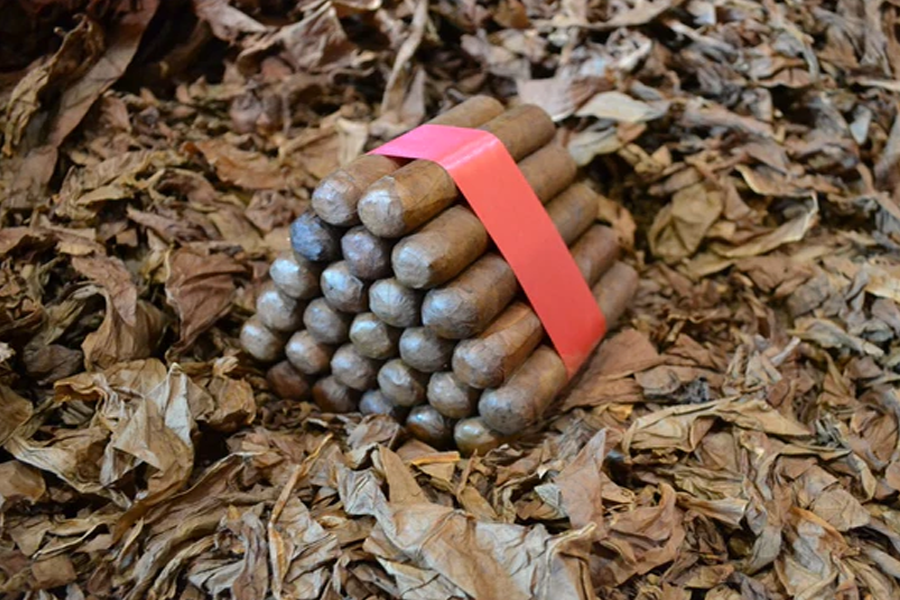 This is a image of a stack of 20 to 25 cigars. They are Rapped together with a thin colored paper ranging from cool whites to firey red wrappings they are forming a trianglur shape simular to a mountain or pyramid. While the Background shows the cigars placed on a feild of tabaco.