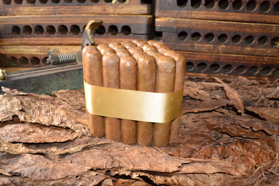 This is a image of a stack of 20 to 25 cigars. They are Rapped together with a thin colored paper ranging from cool whites to firey red wrappings they are forming a trianglur shape simular to a mountain or pyramid. While the Background shows the cigars placed on a feild of tabaco.