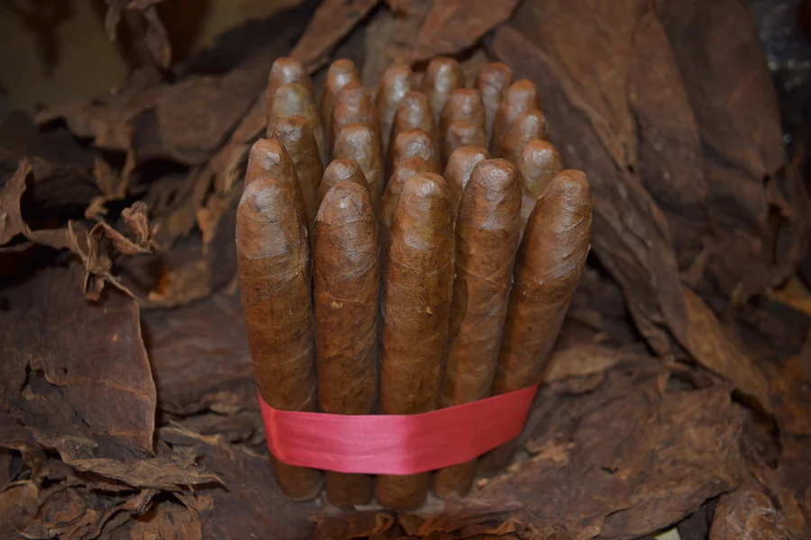 This is a image of a stack of 20 to 25 cigars. They are Rapped together with a thin colored paper ranging from cool whites to firey red wrappings they are forming a square shape simular which resembles a cube. While the Background shows the cigars placed on a feild of tabaco.