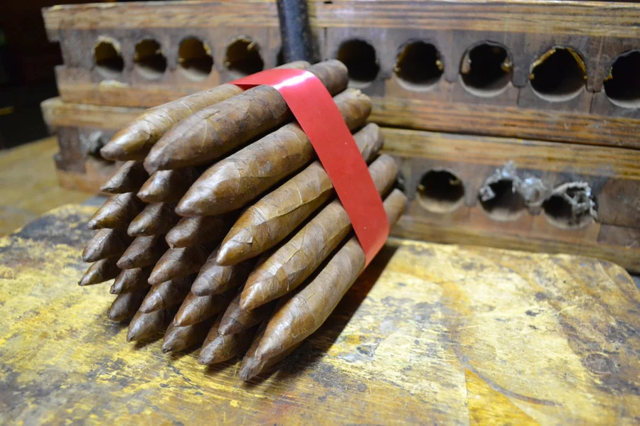 This is a image of a stack of 20 to 25 cigars. They are Rapped together with a thin colored paper ranging from cool whites to firey red wrappings they are forming a trianglur shape simular to a mountain or pyramid. While the Background shows the cigars placed on a feild of tabaco. The tips of the cigars are also very pointy to have a missle like shape hence the name torpedo.