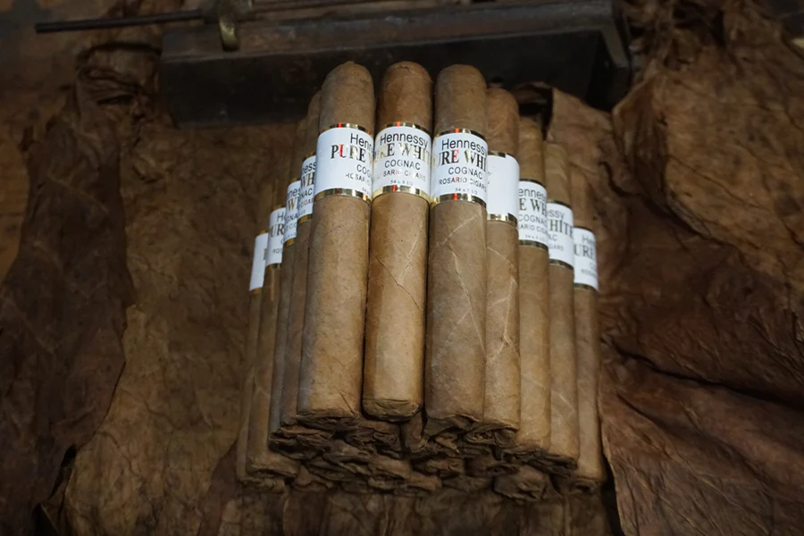 This is a image of a stack of 20 to 25 cigars. They are Rapped together with a thin colored paper ranging from cool whites to firey red wrappings they are forming a trianglur shape simular to a mountain or pyramid. While the Background shows the cigars placed on a feild of tabaco.