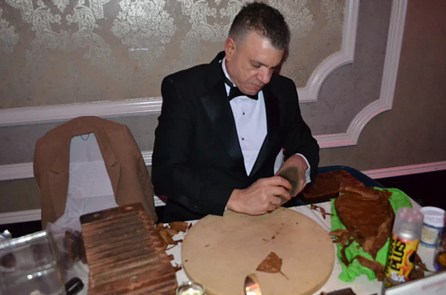 This is a image of a man sitting down. He is handrolling cigars at an even help buy his customerers.