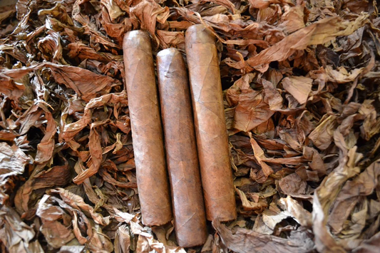 This is a image of a stack of 1 to 5 cigars. They are layed on a of  Background feild of tabaco.