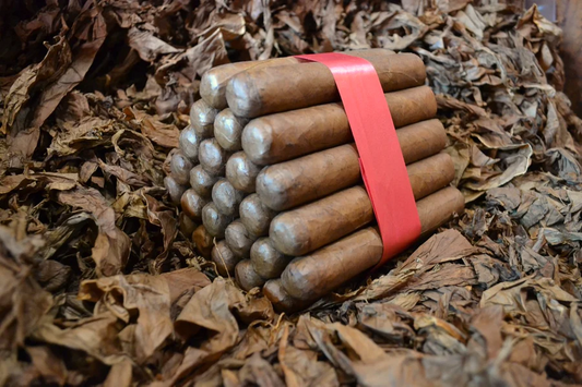 This is a image of a stack of 20 to 25 cigars. They are Rapped together with a thin colored paper ranging from cool whites to firey red wrappings they are forming a trianglur shape simular to a mountain or pyramid. While the Background shows the cigars placed on a feild of tabaco.