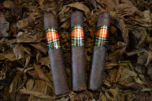 This is a image of a stack of 1 to 5 cigars. They are layed on a of  Background feild of tabaco. the cigars are very dark in color like a dark coffee color.