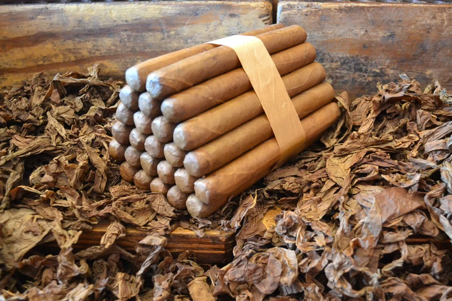 This is a image of a stack of 20 to 25 cigars. They are Rapped together with a thin colored paper ranging from cool whites to firey red wrappings they are forming a trianglur shape simular to a mountain or pyramid. While the Background shows the cigars placed on a feild of tabaco.