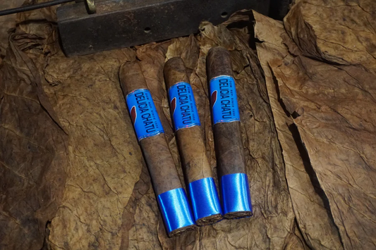 This is a image of a stack of 1 to 5 cigars. They are layed on a of  Background feild of tabaco. The cigars are decoreated wtih a shiny blue wrapper that covers the bottom hald and the mid secotion with two different wrappings.