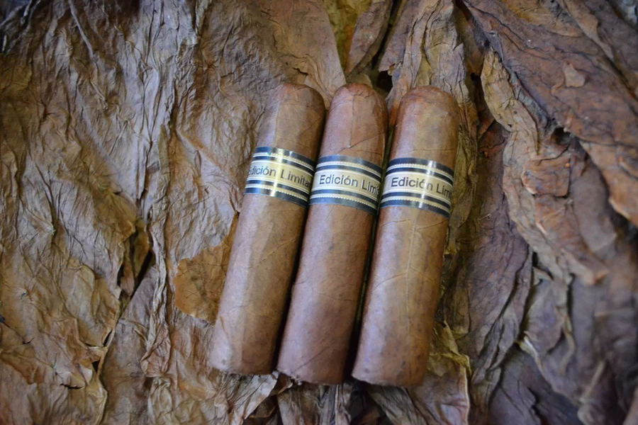 This is a image of a stack of 1 to 5 cigars. They are layed on a of  Background feild of tabaco. These cigars are cool and stubby.