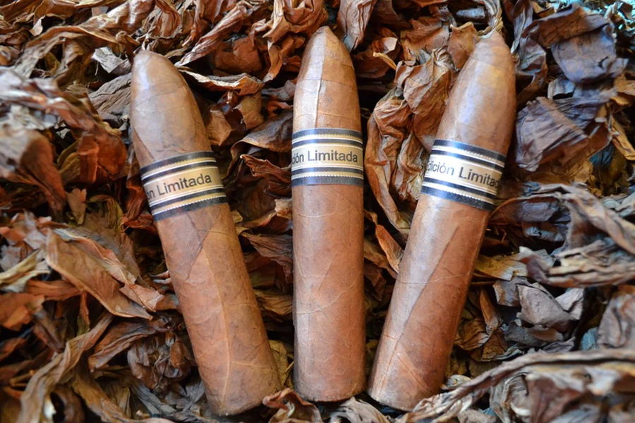 This is a image of a stack of 1 to 5 cigars. They are layed on a of  Background feild of tabaco. The cigars are stubby and pointed at the top.