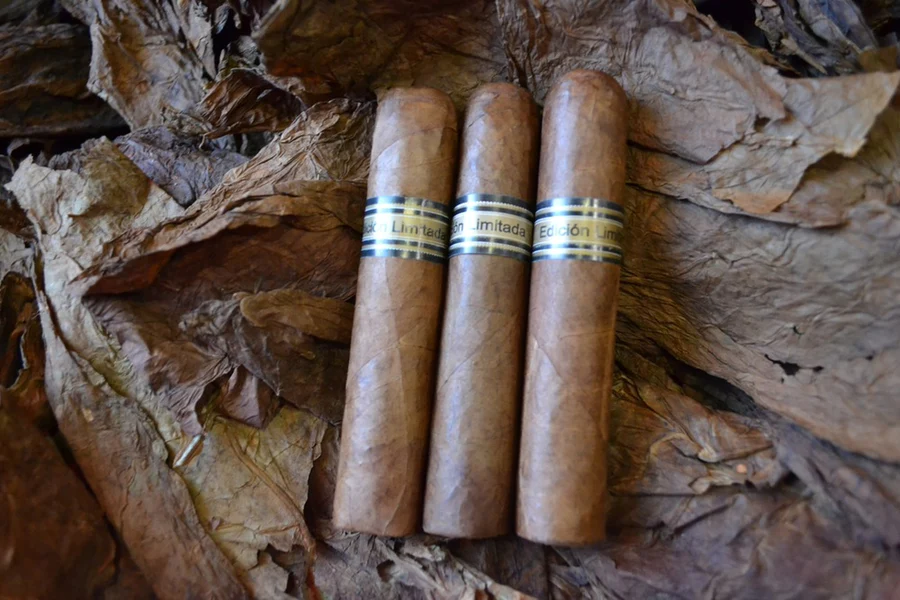This is a image of a stack of 1 to 5 cigars. They are layed on a of  Background feild of tabaco.