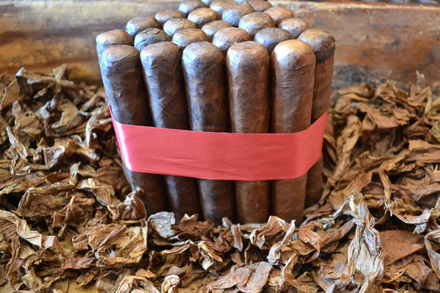 This is a image of a stack of 20 to 25 cigars. They are Rapped together with a thin colored paper ranging from cool whites to firey red wrappings they are forming a trianglur shape simular to a mountain or pyramid. While the Background shows the cigars placed on a feild of tabaco.