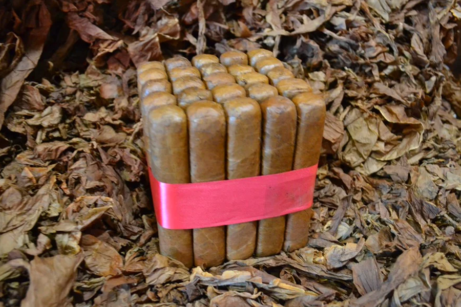 This is a image of a stack of 20 to 25 cigars. They are Rapped together with a thin colored paper ranging from cool whites to firey red wrappings they are forming a square shape simular which resembles a cube. While the Background shows the cigars placed on a feild of tabaco.