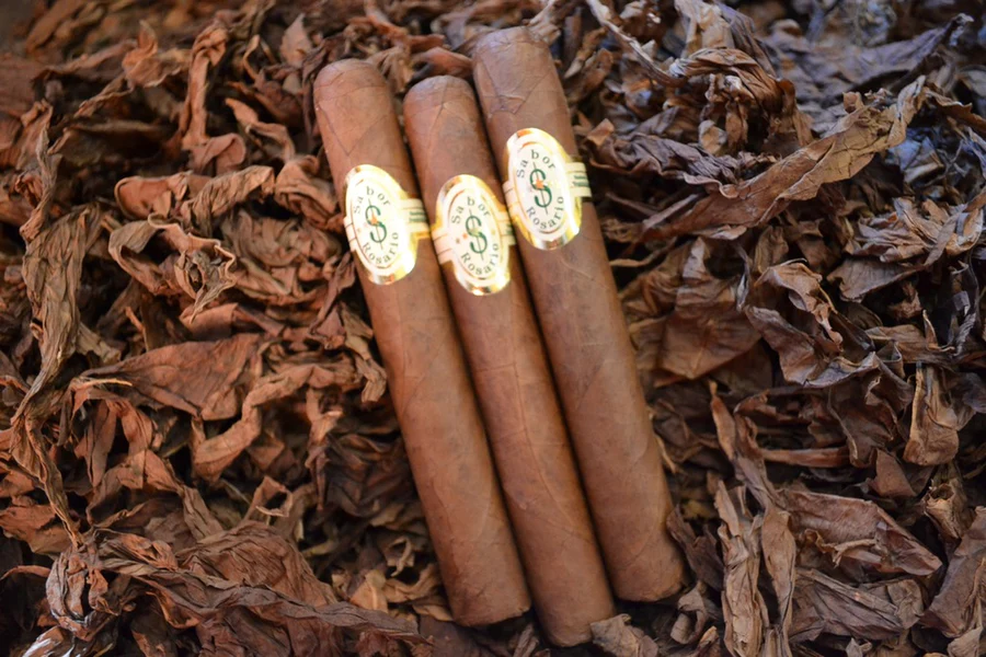 This is a image of a stack of 1 to 5 cigars. They are layed on a of  Background feild of tabaco.