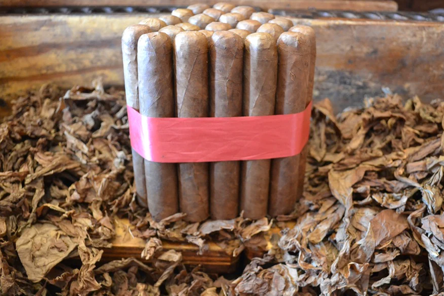 This is a image of a stack of 20 to 25 cigars. They are wrapped together with a thin colored paper ranging from cool whites to firey red wrappings they are forming a triangular shape similar to a mountain or pyramid. While the Background shows the cigars placed on a field of tobacco.