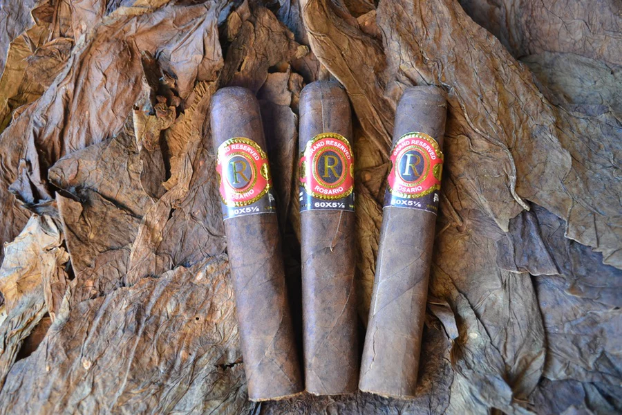 This is a image of a stack of 1 to 5 cigars. They are layed on a of  Background feild of tabaco. these cigars are colored in a smoky texture.