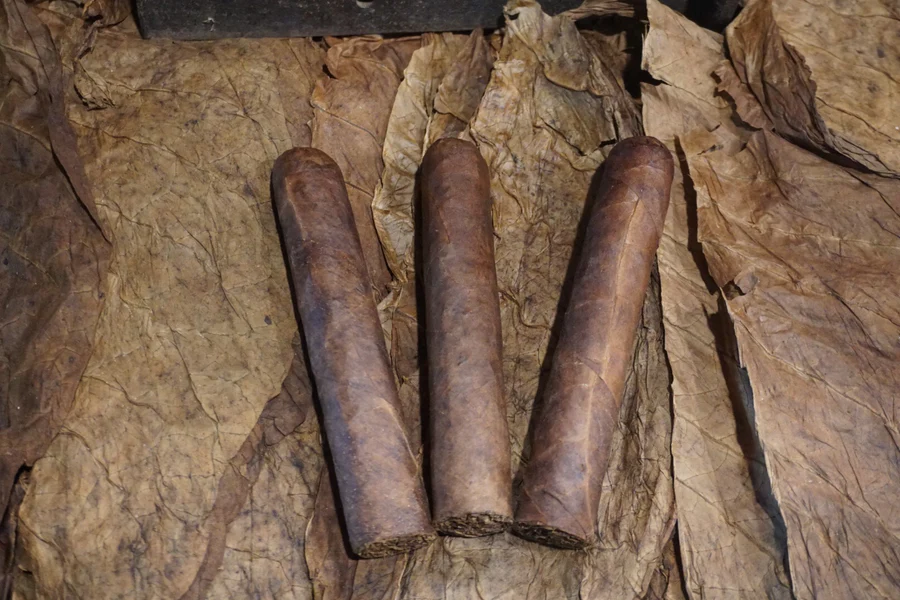 This is a image of a stack of 1 to 5 cigars. They are layed on a of  Background feild of tabaco.