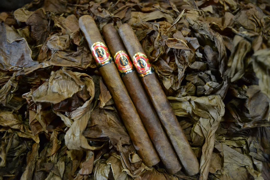 This is a image of a stack of 1 to 5 cigars. They are layed on a of  Background feild of tabaco. These cigars are long and slim.