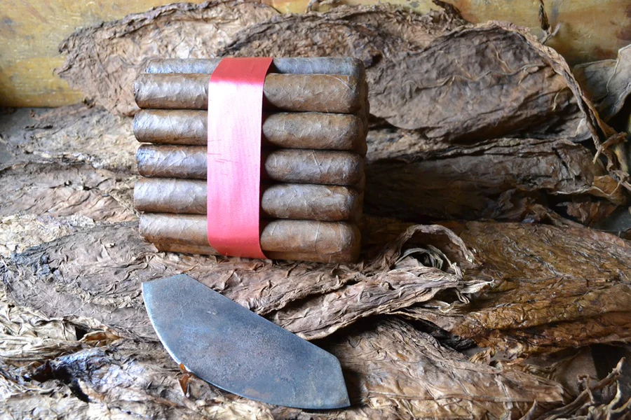 This is a image of a stack of 20 to 25 cigars. They are Rapped together with a thin colored paper ranging from cool whites to firey red wrappings they are forming a trianglur shape simular to a mountain or pyramid. While the Background shows the cigars placed on a feild of tabaco.