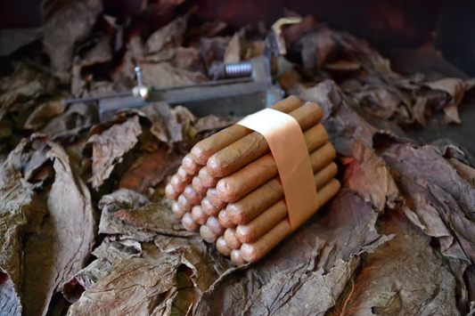 This is a image of a stack of 20 to 25 cigars. They are Rapped together with a thin colored paper ranging from cool whites to firey red wrappings they are forming a trianglur shape simular to a mountain or pyramid. While the Background shows the cigars placed on a feild of tabaco.