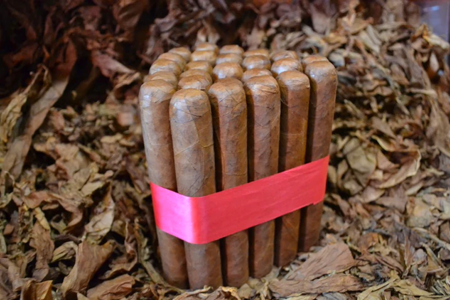 This is a image of a stack of 20 to 25 cigars. They are Rapped together with a thin colored paper ranging from cool whites to firey red wrappings they are forming a trianglur shape simular to a mountain or pyramid. While the Background shows the cigars placed on a feild of tabaco.