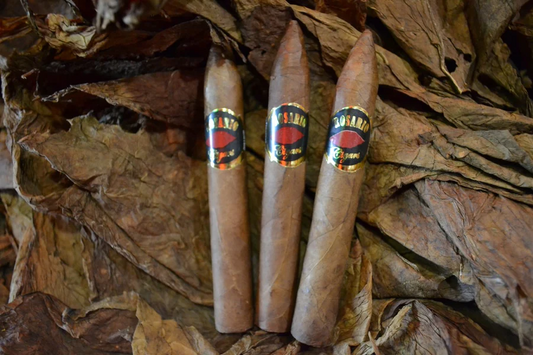This is a image of a stack of 1 to 5 cigars. They are layed on a of  Background feild of tabaco. These cigars also have a pointy top.
