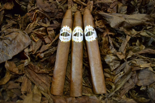 This is a image of a stack of 1 to 5 cigars. They are layed on a of  Background feild of tabaco. These cigars also have a pointy top.