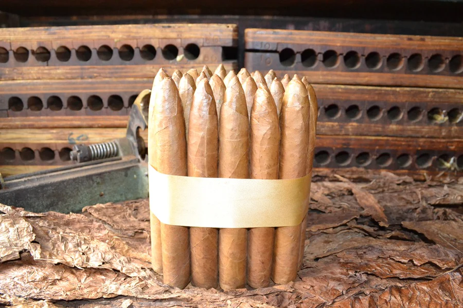 This is a image of a stack of 20 to 25 cigars. They are Rapped together with a thin colored paper ranging from cool whites to firey red wrappings they are forming a square shape simular which resembles a cube. While the Background shows the cigars placed on a feild of tabaco. The tips of the cigars are also very pointy to have a missle like shape hence the name torpedo.